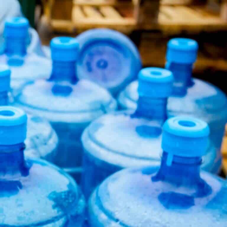 Big empty plastic water bottles for the cooler are stacked at outdoor warehouse.