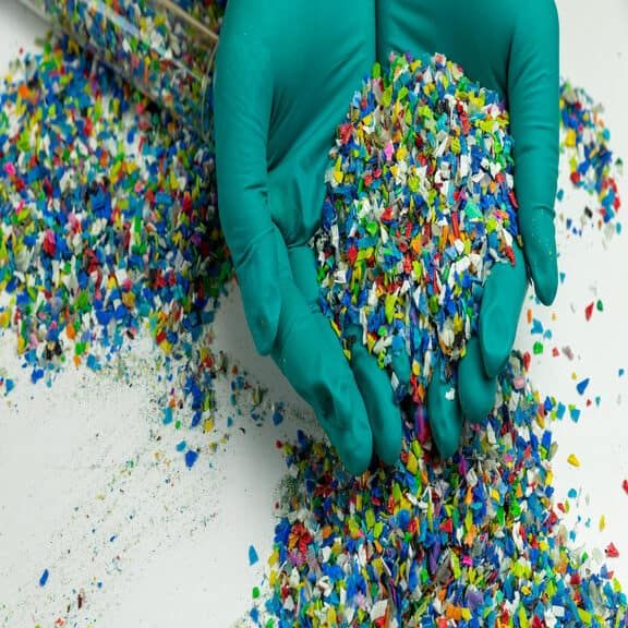 Crushed plastic on green gloved hand. Reuse of plastic. polymer beads. Scraps obtained from plastic waste. The world